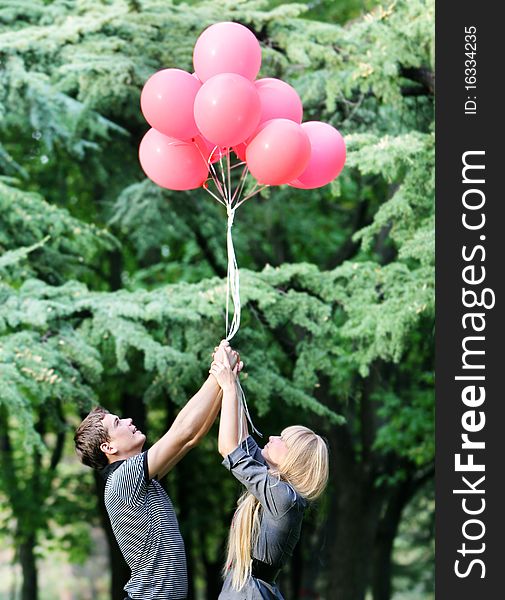 Young loving couple with red balloons on natural background