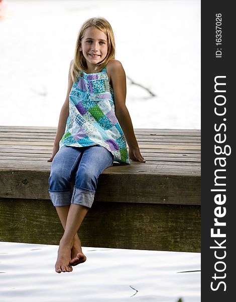 A young, pretty, preadolescent sitting on a dock and smiling at the camera. A young, pretty, preadolescent sitting on a dock and smiling at the camera.