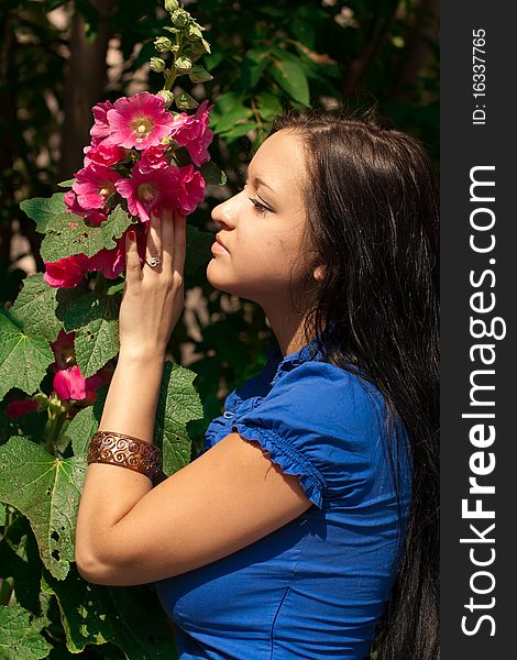 Beautiful girl with long dark hair, in blue shirt with red flower in a sunny park. Beautiful girl with long dark hair, in blue shirt with red flower in a sunny park