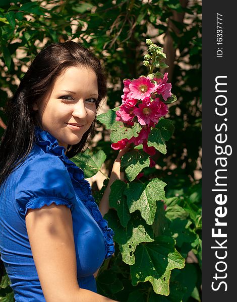 Beautiful girl with long dark hair, in blue shirt with red flower in a sunny park. Beautiful girl with long dark hair, in blue shirt with red flower in a sunny park