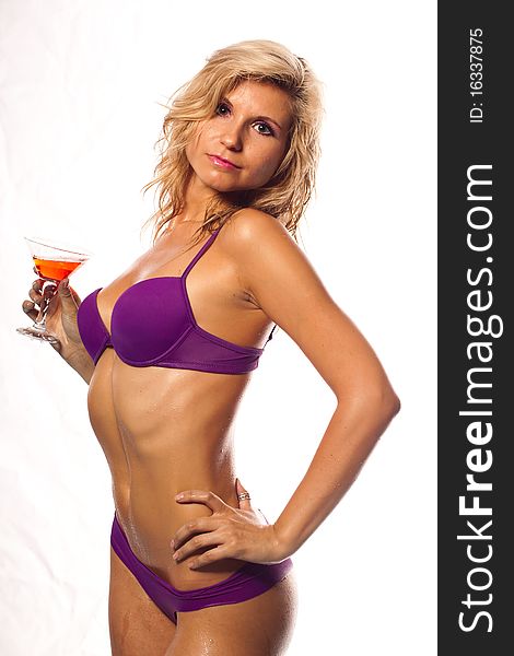 Beautiful sexy girl in a wet violet bikini with glass of wine in the drops of water. She is in studio isolated on a white background. Beautiful sexy girl in a wet violet bikini with glass of wine in the drops of water. She is in studio isolated on a white background