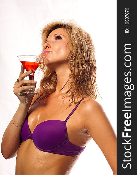 Beautiful girl in a wet violet bikini with glass of wine in the drops of water. She is in studio isolated on a white background. Beautiful girl in a wet violet bikini with glass of wine in the drops of water. She is in studio isolated on a white background