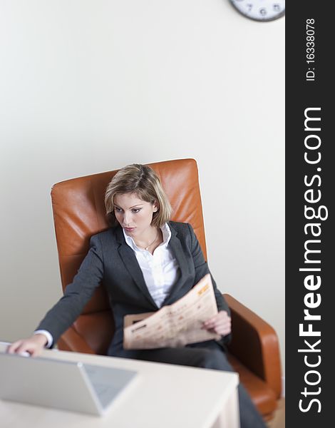 Business woman working on her laptop, holding a newspaper