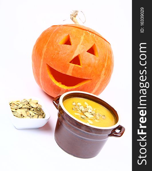 Pumpkin soup decorated with pumpkin seeds and Jack-o'-lantern in the background