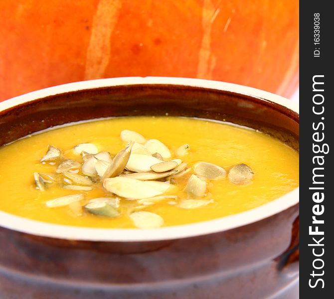 Pumpkin soup decorated with pumpkin seeds a pumpkin in the background