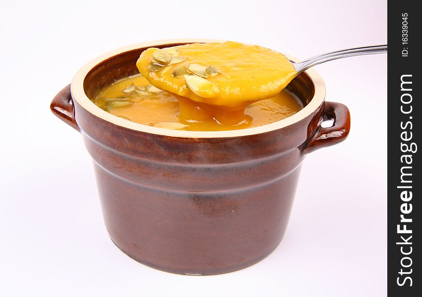 Pumpkin soup decorated with pumpkin seeds being eaten with a spoon