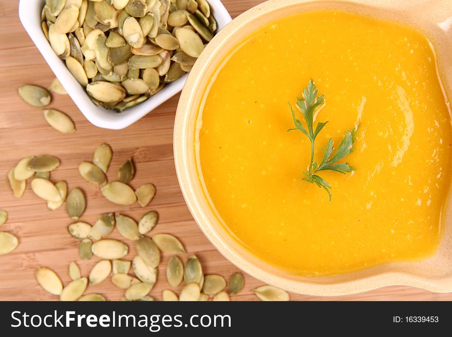 Pumpkin soup decorated with parsley and a bowl of pumpkin seeds on wooden background