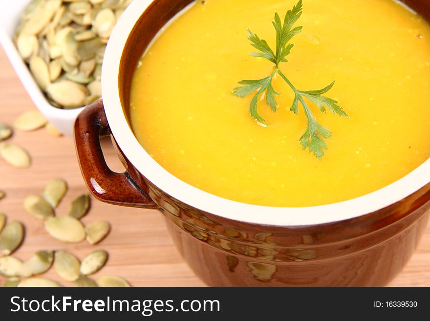 Pumpkin soup decorated with parsley and a bowl of pumpkin seeds on wooden background. Pumpkin soup decorated with parsley and a bowl of pumpkin seeds on wooden background