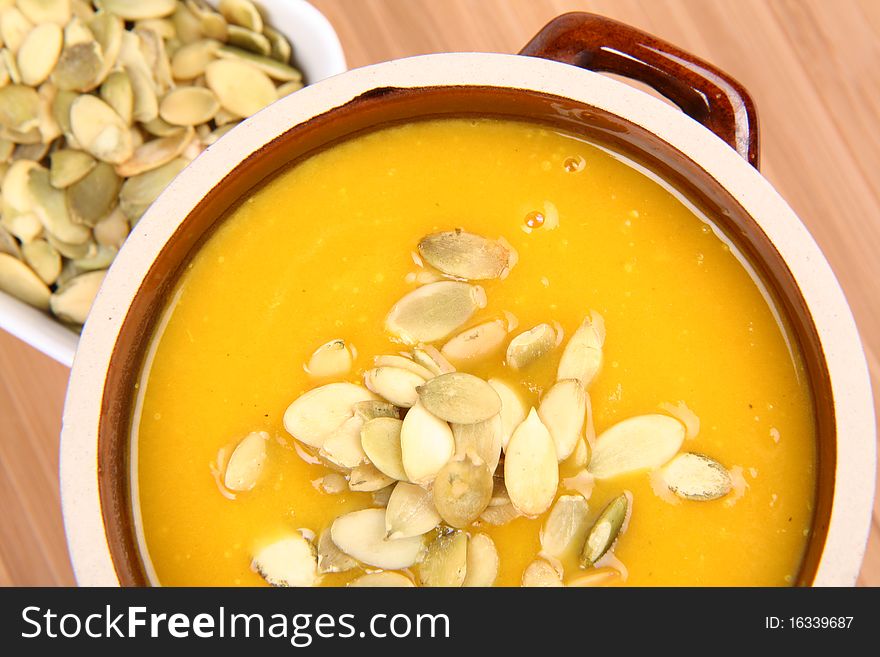 Pumpkin soup and a bowl of pumpkin seeds on wooden background