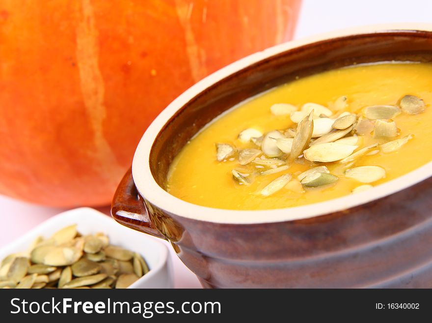 Pumpkin soup decorated with pumpkin seeds and a bowl of seeds and a pumpkin in the background