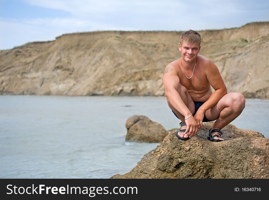 Smiling Young Man Is Squatting On The Rock