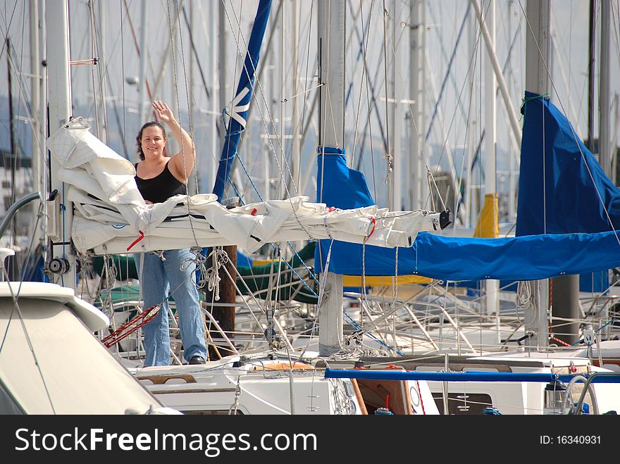 A woman stands on her sailboat near the main mast and waves to her guests to come aboard. A woman stands on her sailboat near the main mast and waves to her guests to come aboard