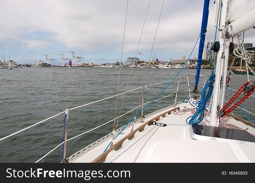 A sloop under way with the main sail only near the San Francisco Bay with Jack London Square in the background. A sloop under way with the main sail only near the San Francisco Bay with Jack London Square in the background