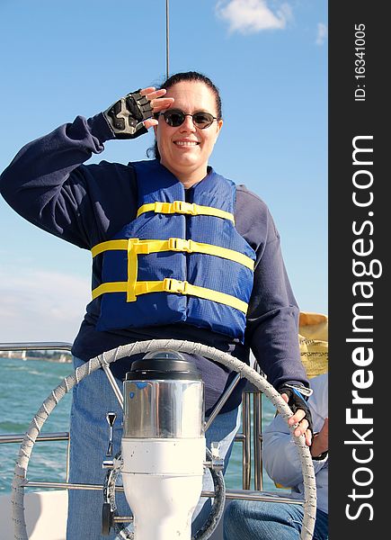 A happy woman sailing on the ocean handles the sailboat and salutes with a smile. A happy woman sailing on the ocean handles the sailboat and salutes with a smile