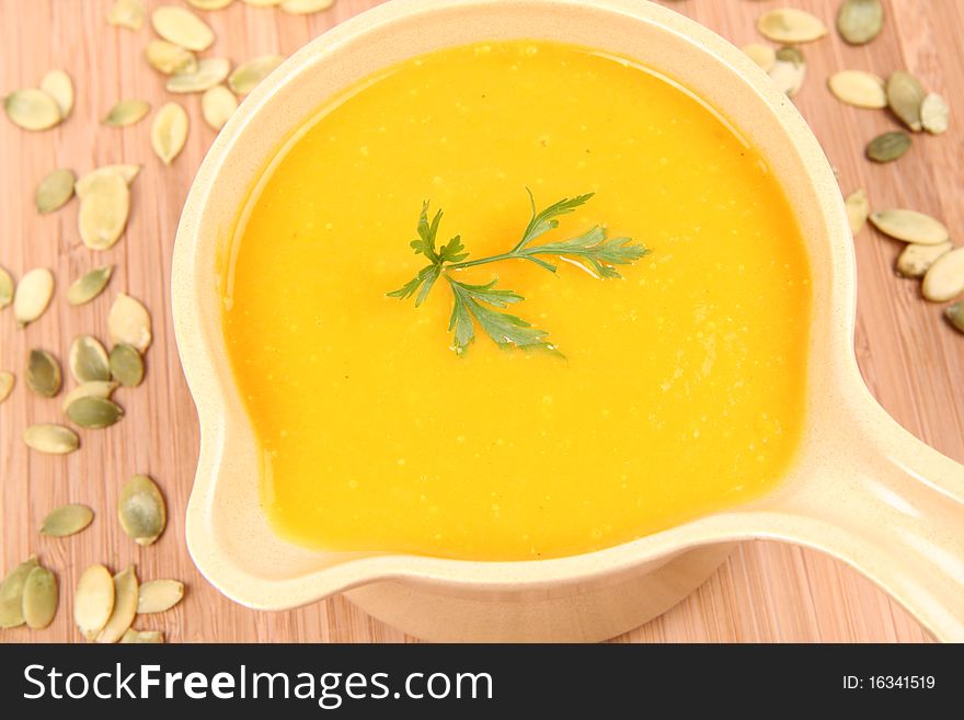 Pumpkin soup decorated with parsley and some pumpkin seeds on wooden background