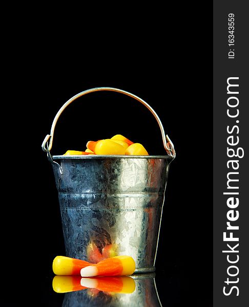 Bucket of candy corn on a black background with reflection