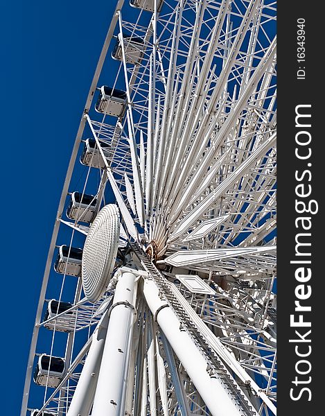 A large white ferris wheel with enclosed cars shot from below with a deep blue sky in the background.