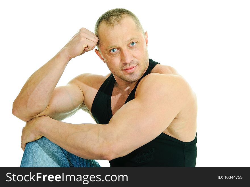Man bodybuilder in jeans and black sleeveless sits on white background. Man bodybuilder in jeans and black sleeveless sits on white background