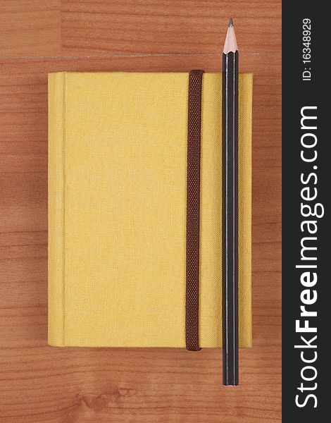 Yellow book with pencil on wood background. Yellow book with pencil on wood background