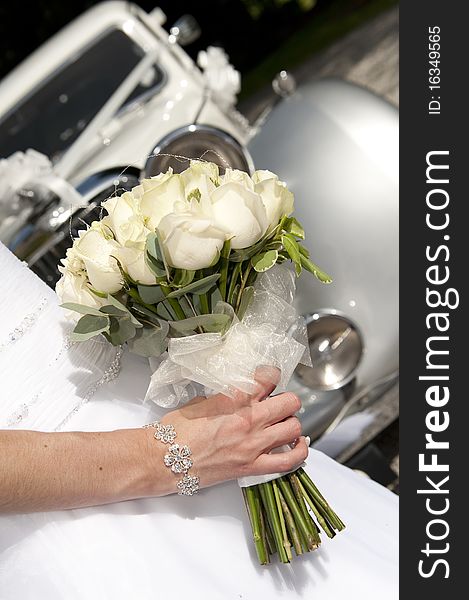 A bride's boquet of ceream roses with a vintage wedding car in the background