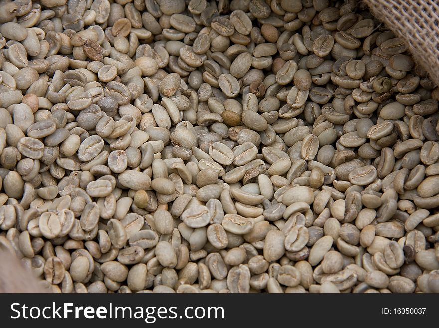 Many grains of green coffee lie in a sack. Many grains of green coffee lie in a sack