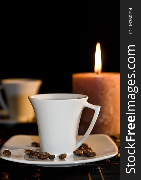 Candle and cups of coffe on the table on the black background. Candle and cups of coffe on the table on the black background.