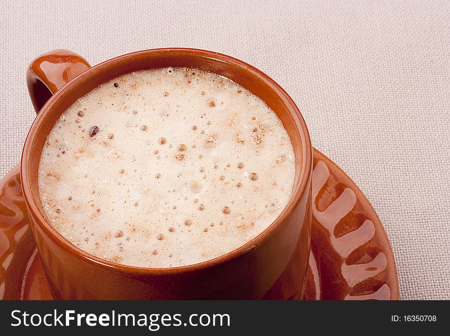 Cappuccino in a brown ceramic cup with a saucer.