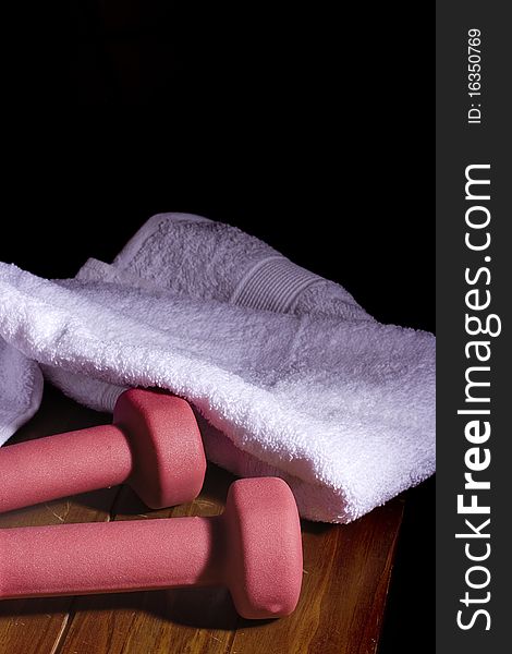 Two pink dumbbells laying next to a white towel on a wooden surface.