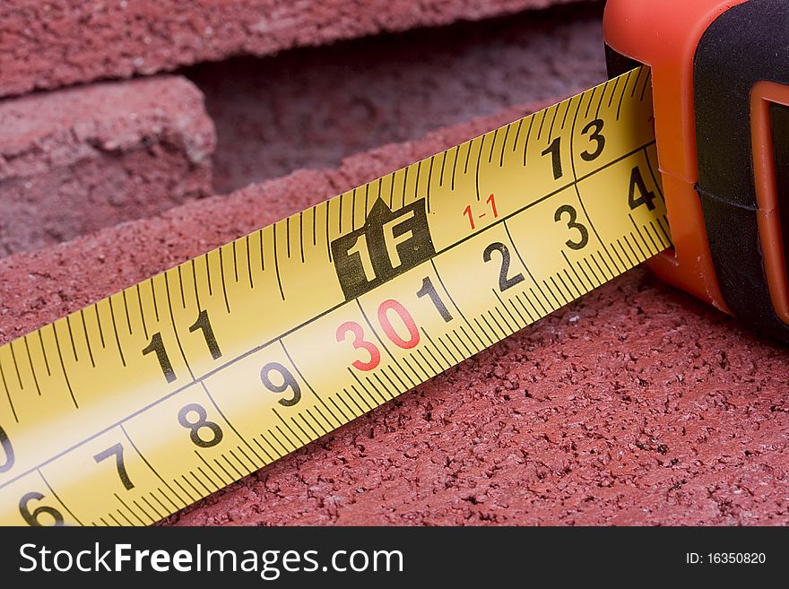 Orange tape measure on a red brick.