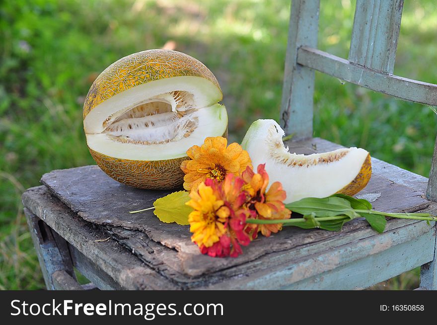 The cut melon lies on a chair, alongside three flowers. The cut melon lies on a chair, alongside three flowers