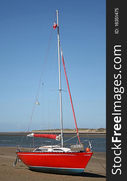 Lovely red yacht on the beach with a for sale sign on the bow, with views over the estuary and sandbanks, under a beautiful blue sky. Lovely red yacht on the beach with a for sale sign on the bow, with views over the estuary and sandbanks, under a beautiful blue sky.