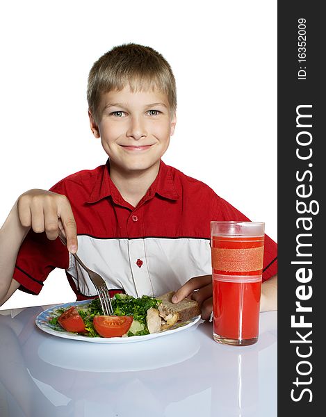 The teenager has breakfast. On a table a plate with vegetables and glass of juice.