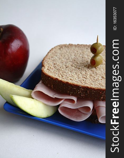 Ham sandwich on whole wheat bread garnished with olives and apple slices.