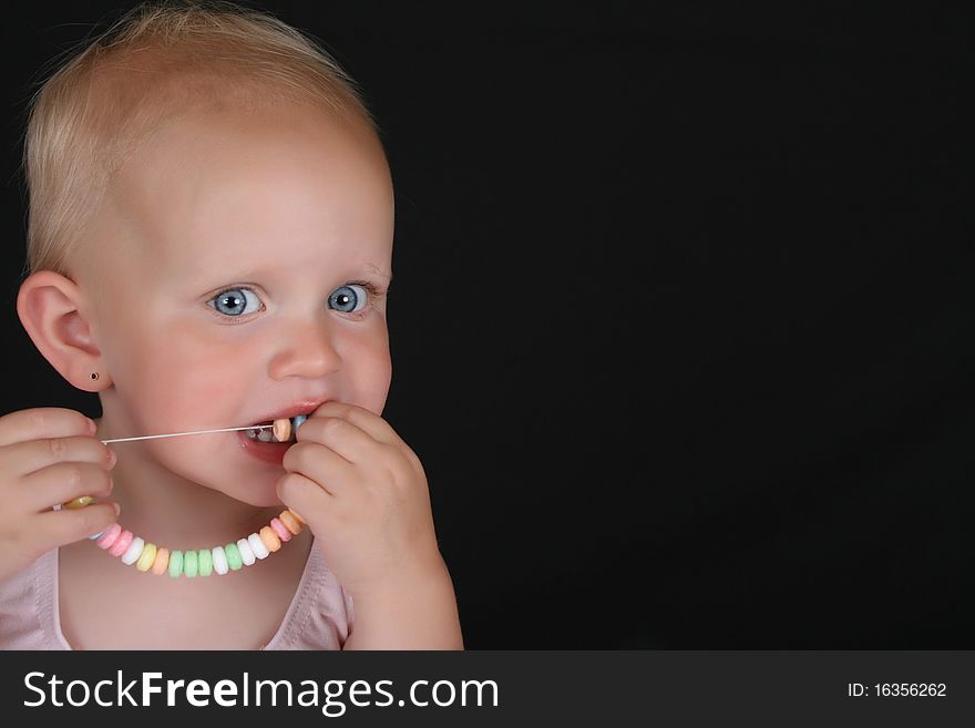 Cute blond toddler eating a candy necklace. Cute blond toddler eating a candy necklace