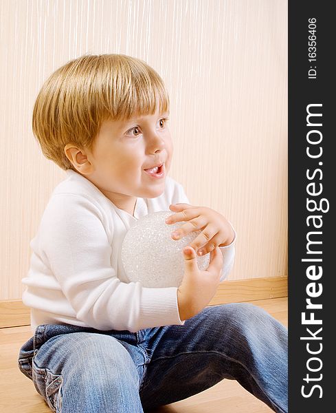 The child sitting on the wood floor with white ball. The child sitting on the wood floor with white ball