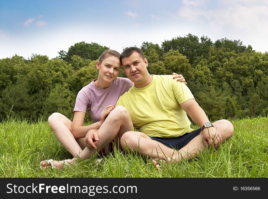 Young couple sitting on the grass in the summer park