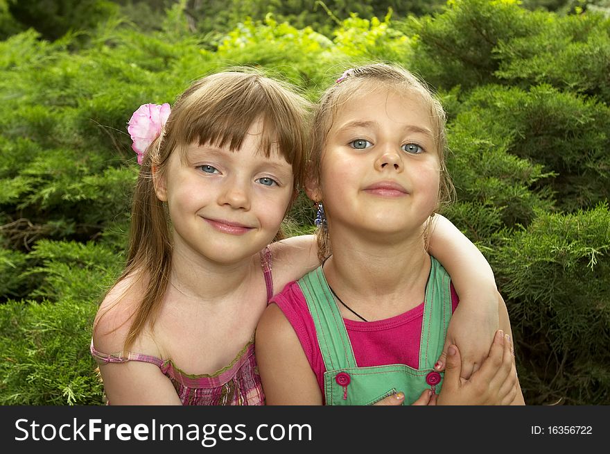 Two little girls standing together in the park, one hugs another