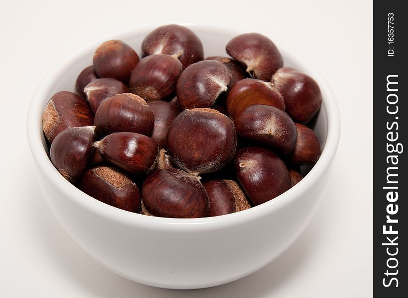 A bowl of raw chestnuts isolated on a white background. A bowl of raw chestnuts isolated on a white background.