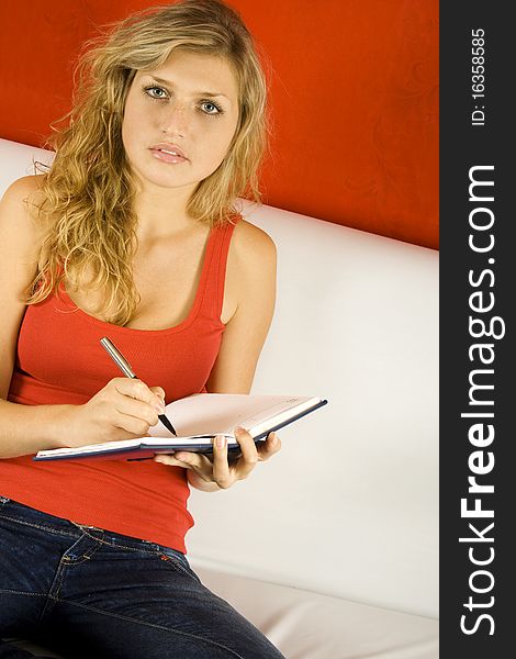 Young woman sitting on the couch and makes entries in the phonebook. Young woman sitting on the couch and makes entries in the phonebook
