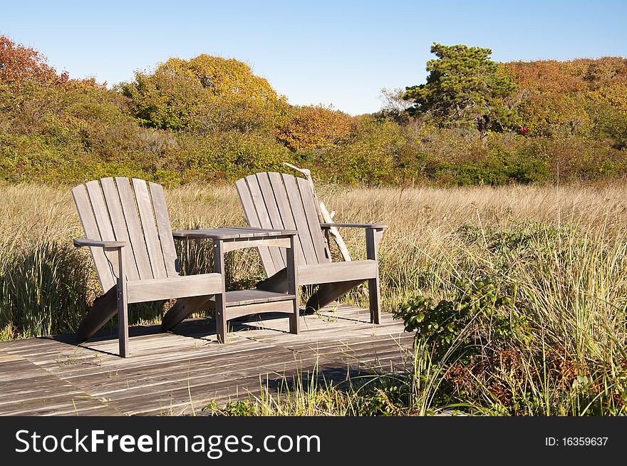 Two Adirondack chairs sit on a simple deck against the beginnings of fall foliage. Two Adirondack chairs sit on a simple deck against the beginnings of fall foliage.