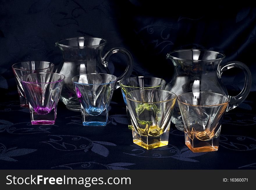 Colored glass jug and glasses on a dark background. Colored glass jug and glasses on a dark background