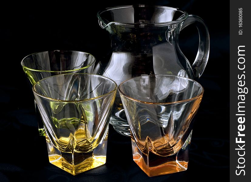 Colored glass jug and glasses on a dark background. Colored glass jug and glasses on a dark background