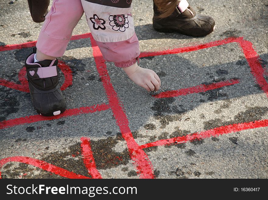 Up close shot of a little girl picking up her rock in hopscotch. Up close shot of a little girl picking up her rock in hopscotch