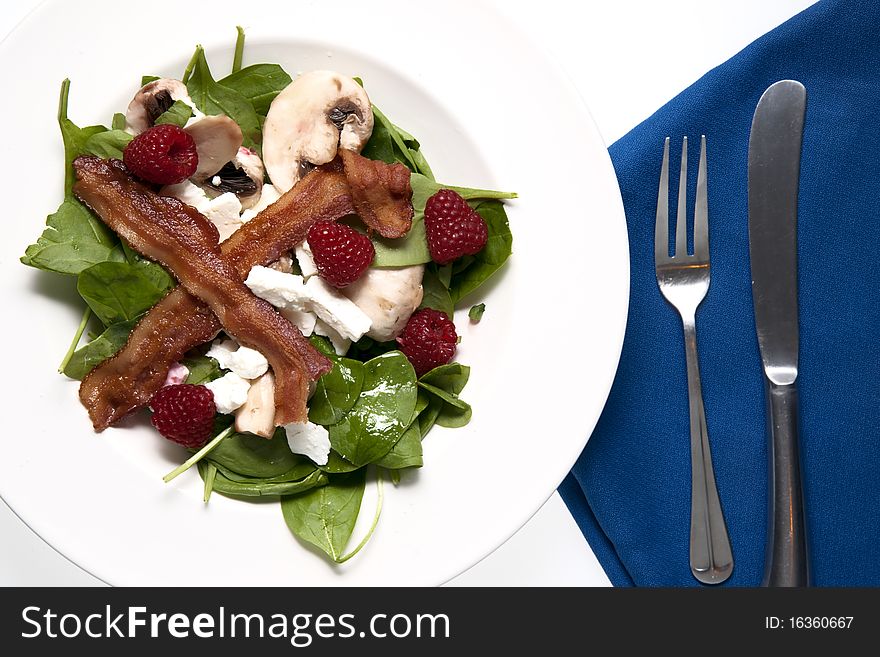 A delicious spinach and bacon salad garnished with cheese, mushroom and berries. A delicious spinach and bacon salad garnished with cheese, mushroom and berries