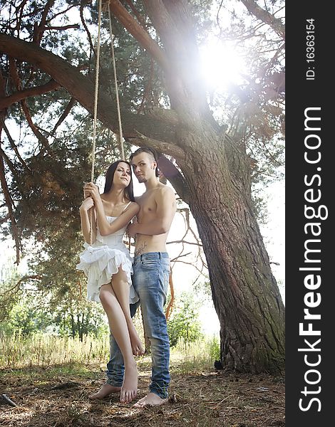 Young happy smiling embracing couple swinging outdoor in nature. Young happy smiling embracing couple swinging outdoor in nature