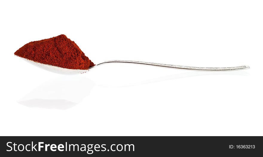 Silver spoon containing spicy paprika powder on a white background with reflections