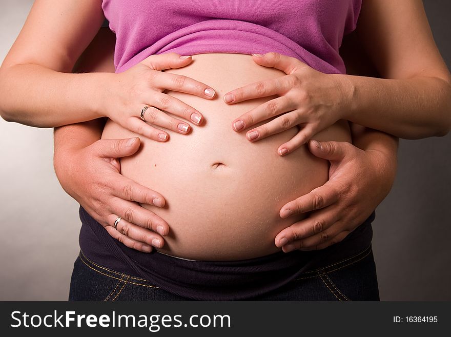 Foto of pregnant woman and her husband is in a studio. Hug a stomach hands