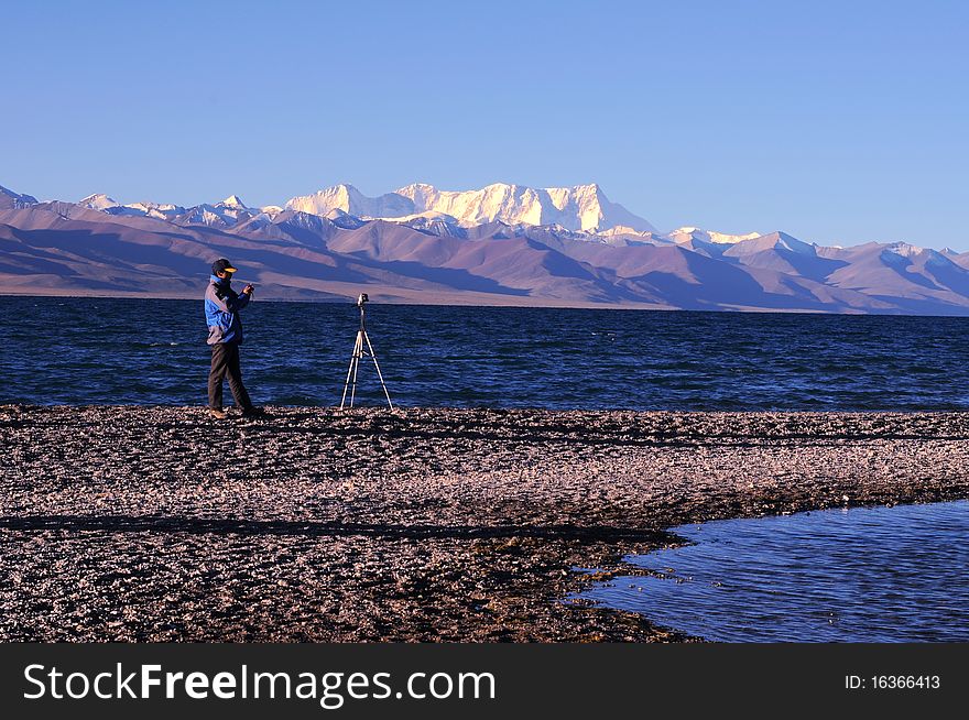 Portrait of a photographer shooting at sunrise at the bank of a blue lake in Tibet.