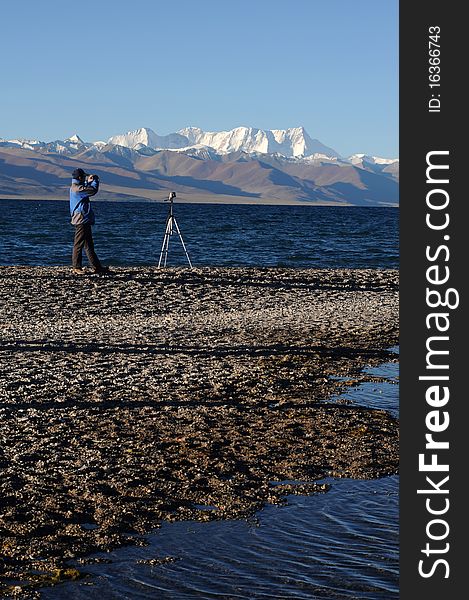 Portrait of a photographer shooting at sunrise at the bank of a blue lake in Tibet.