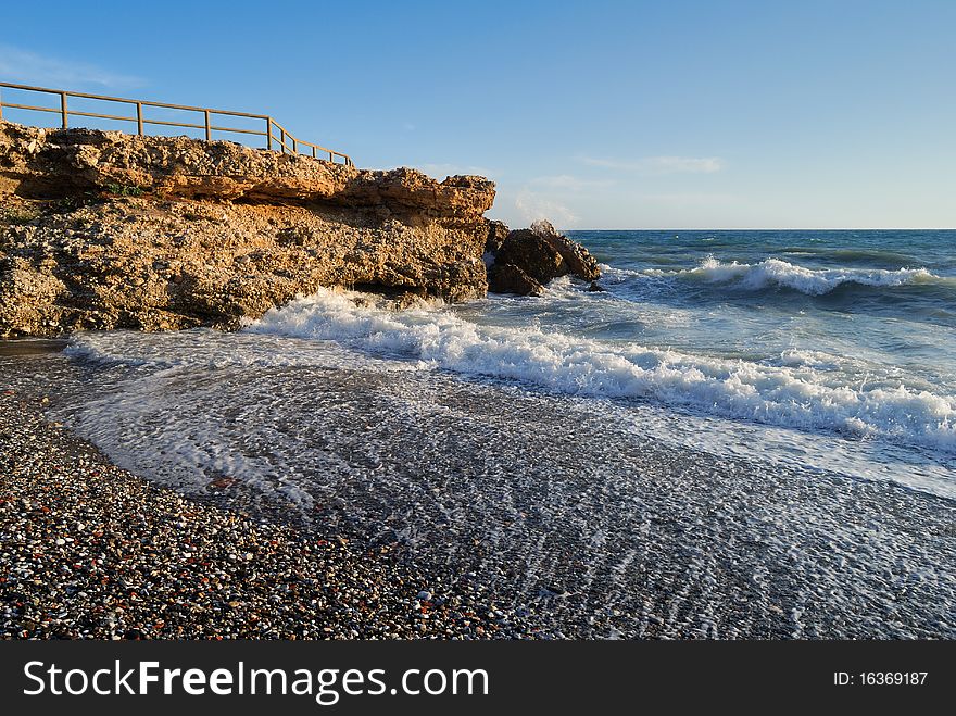 Late afternoon shot of a secluded beach spot at the Costa del Sol. Waves come rolling onto the colourful stone beach as tranquility sets in after the day's vibrant beach life.